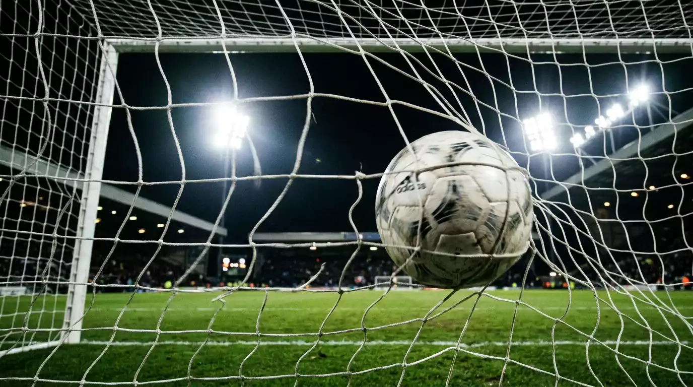Balón de fútbol golpeando la red de la portería bajo los focos nocturnos del estadio
